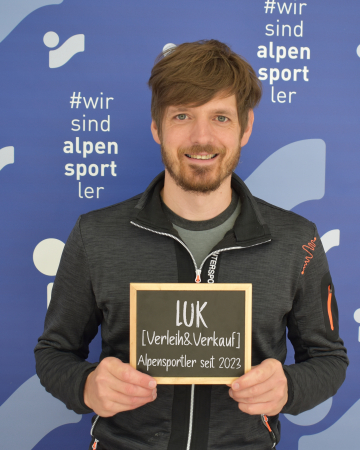 Mann hält Schild für Luk Alpensportler Skiverleih und -verkauf
