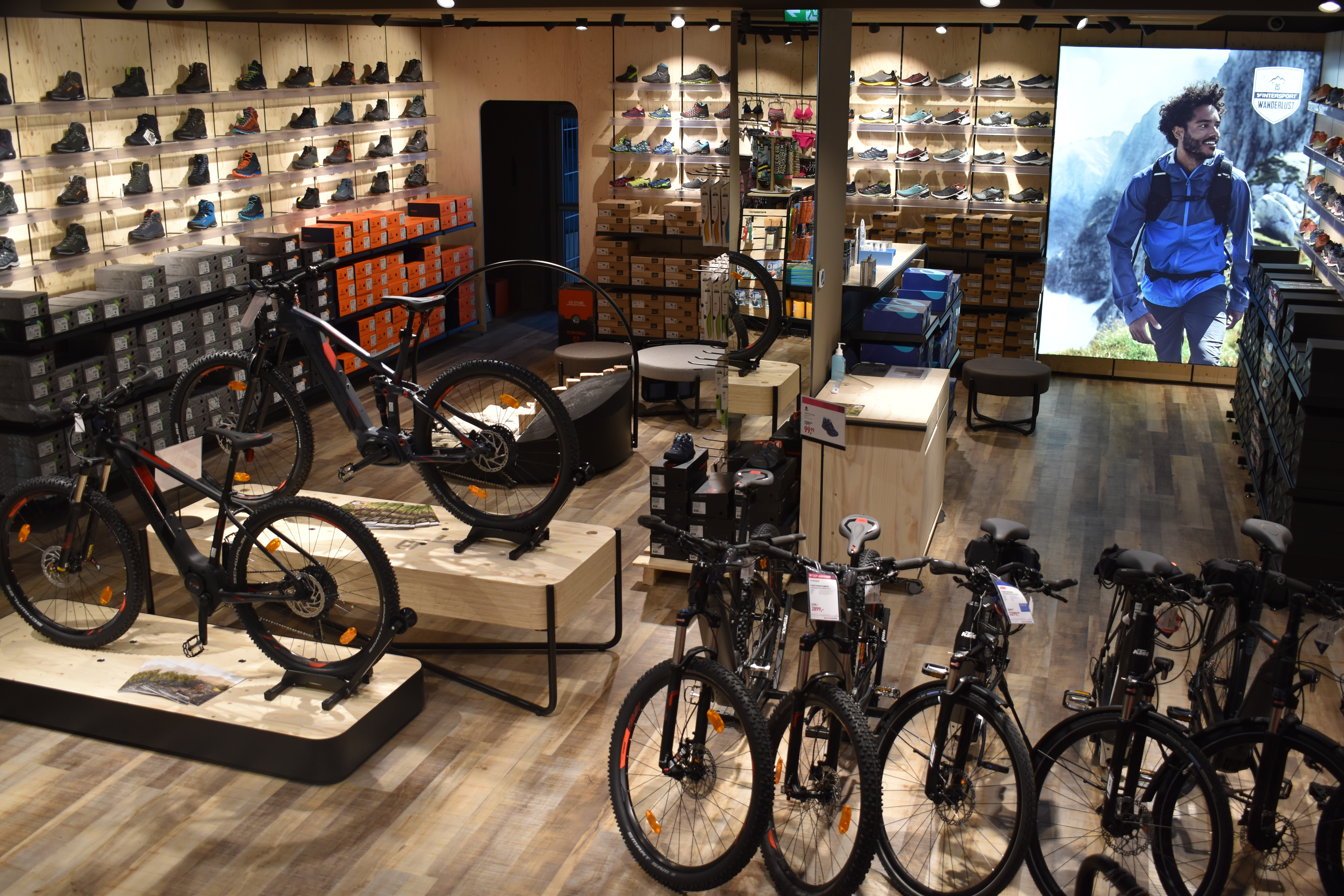 Innenraum eines Outdoor-Ausrüstungsgeschäfts mit Mountainbikes, Wanderschuhen und Bekleidungsauslage.