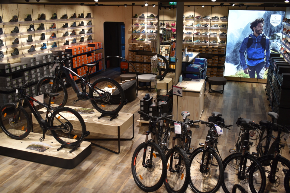 Innenraum eines Outdoor-Ausrüstungsgeschäfts mit Mountainbikes, Wanderschuhen und Bekleidungsauslage.
