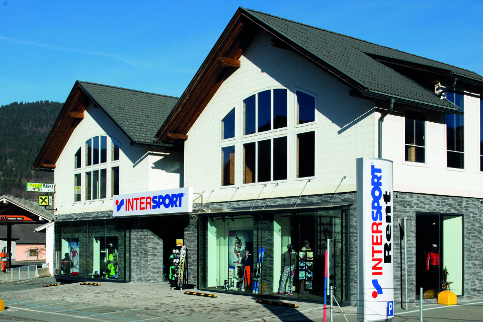 Außenansicht des Intersport-Skiverleihs; Wintersportgeschäft mit großen Fenstern und Beschilderung.