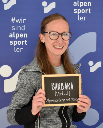 Lächelnde Frau hält ein "Barbara Verkauf" Schild für den Alpensportler Ski Shop.