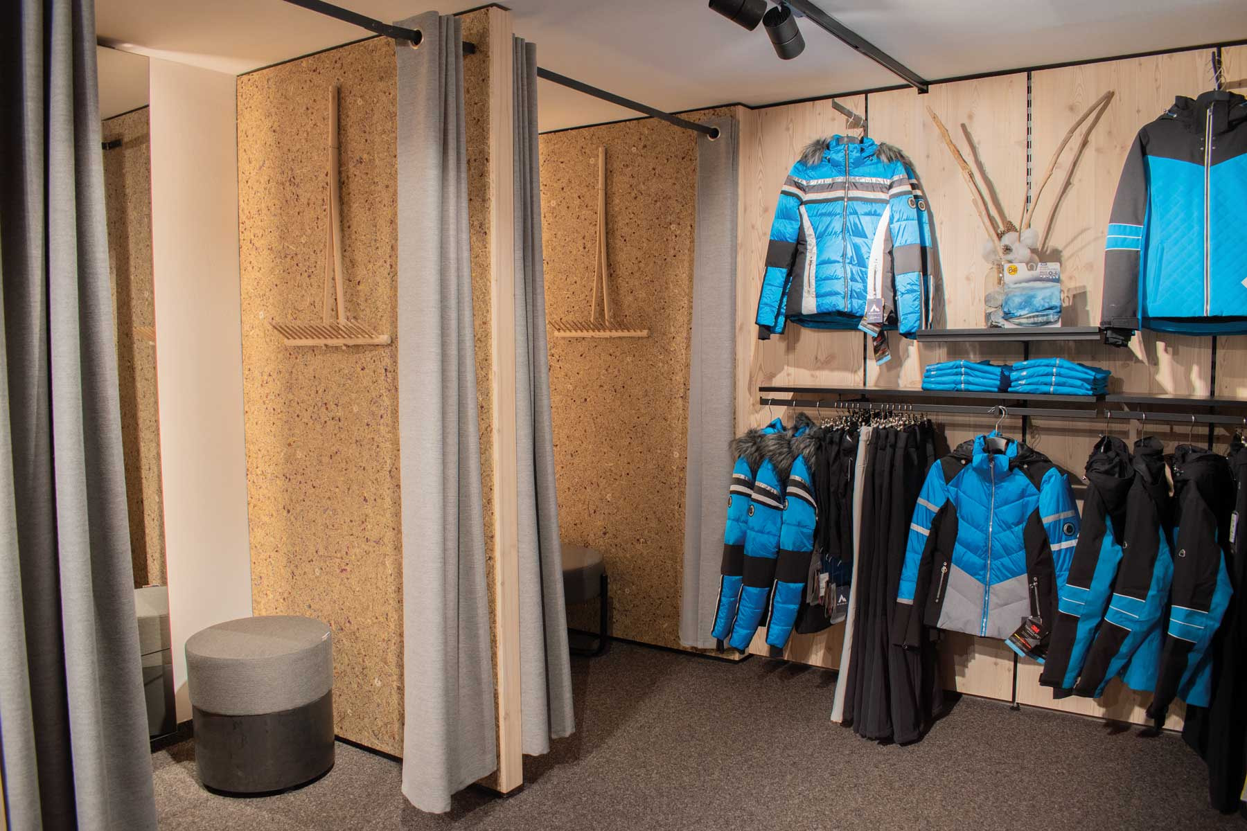 Innenraum eines Skigeschäfts mit Umkleidekabinen, Winterjacken und Bekleidung auf Ausstellungsregalen.