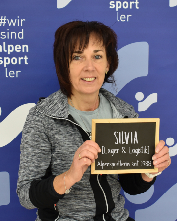 Silvia, Logistikmitarbeiterin und Alpensportlerin seit 1988, hält ein Schild.