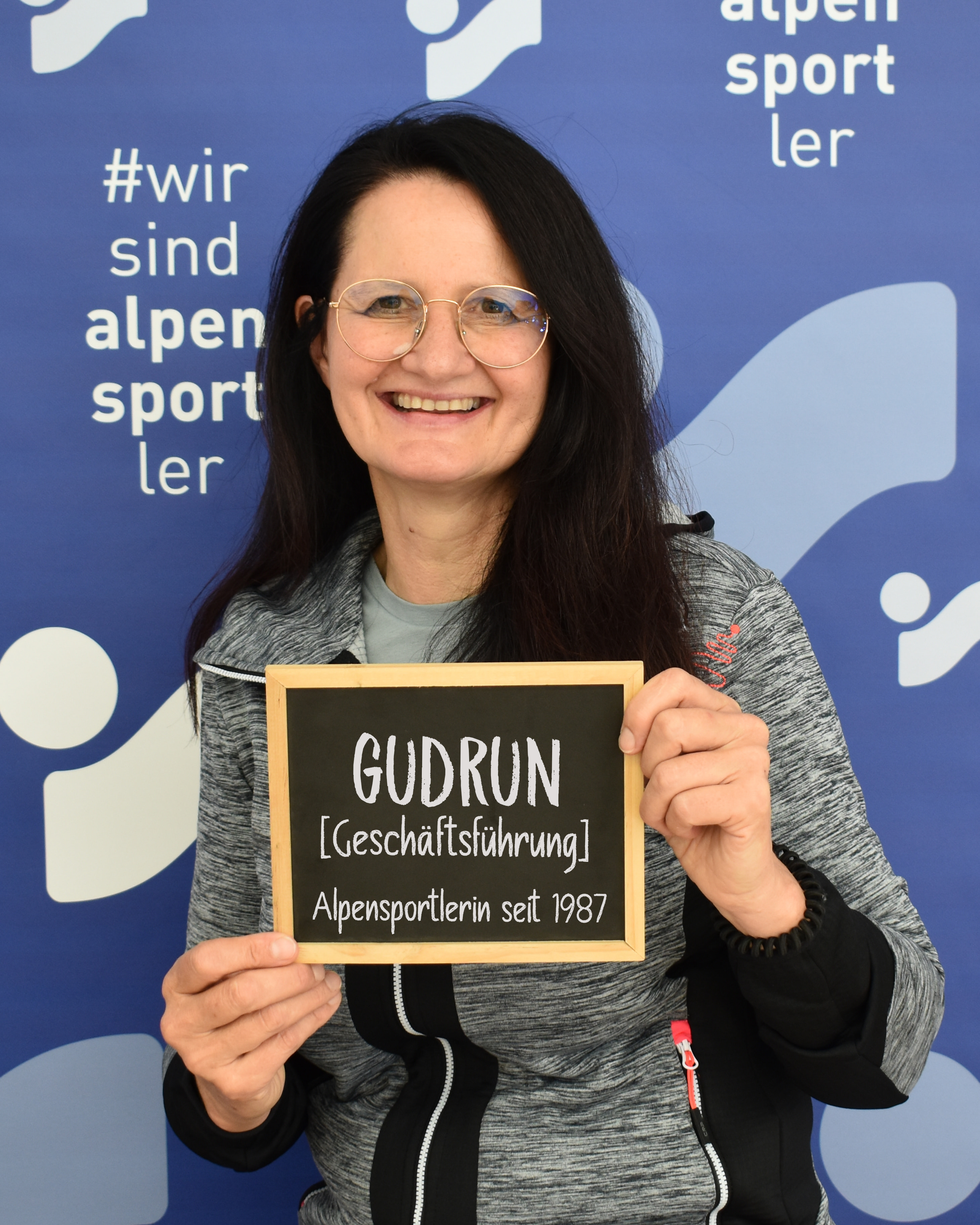Gudrun, Leiterin von Alpensportler, hält ein Schild mit ihrem Namen und Titel. Alpensportler seit 1987.
