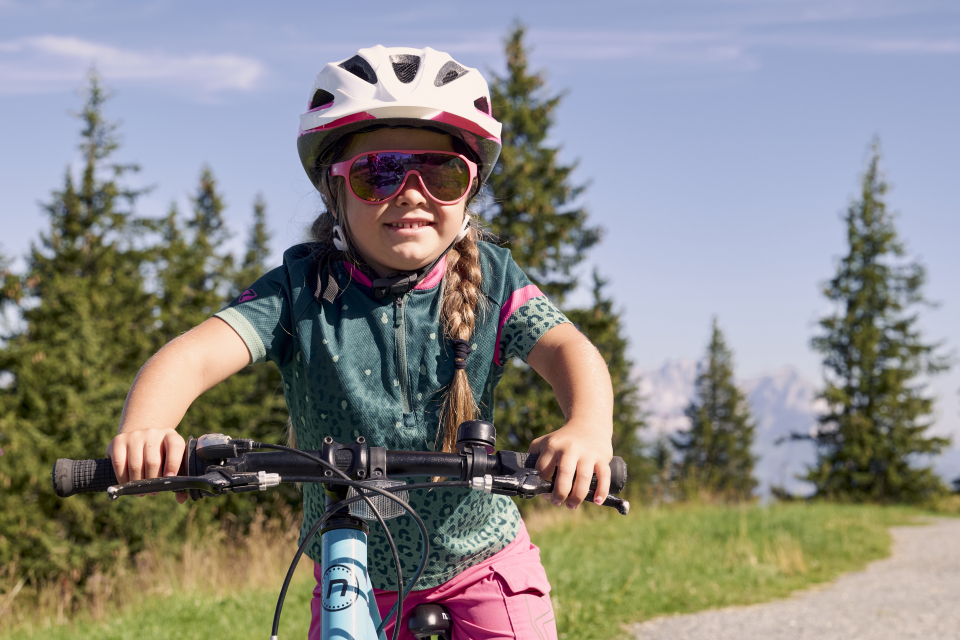 Radfahrerin mit Helm und Sonnenbrille, die an einem sonnigen Tag im Freien Fahrrad fährt.