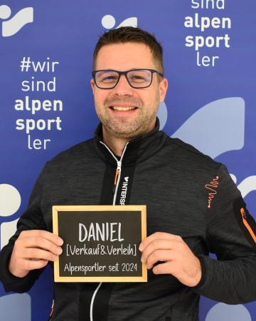 Lächelnder Mann hält ein Schild für Daniel, Alpensportler Skiverleih und Verkauf.
