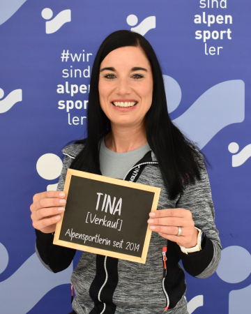 Lächelnde Frau hält "Tina Verkauf" Schild für Alpensport Team-Mitgliederprofil.
