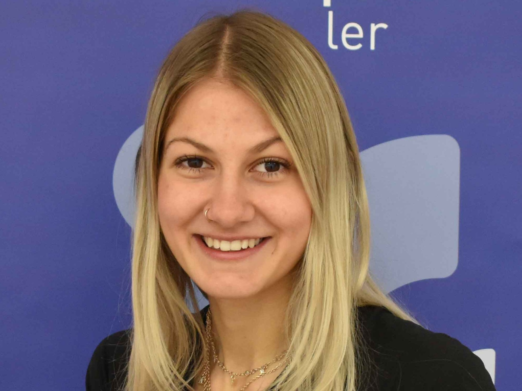 Porträt einer lächelnden jungen Frau mit blonden Haaren vor blauem Hintergrund.