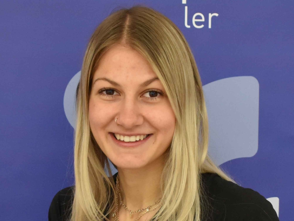 Porträt einer lächelnden jungen Frau mit blonden Haaren vor blauem Hintergrund.