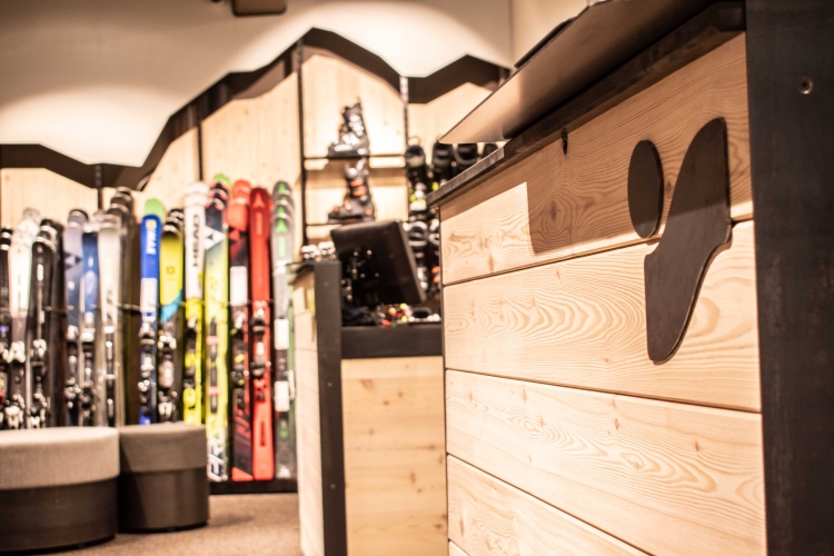 Innenausstattung eines Skigeschäfts mit Skiern, Skischuhen und einer Holztheke mit einem Ausschnittdesign in Form eines Skischuhs.