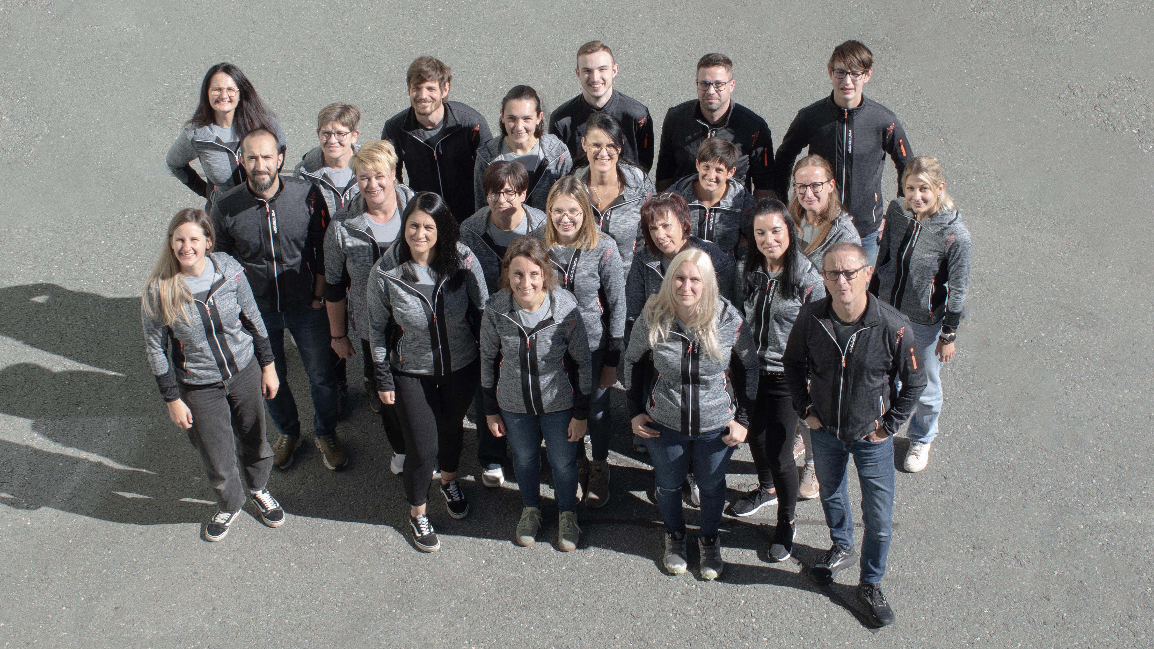 Gruppenporträt verschiedener Teammitglieder in passenden grauen Jacken, Firmenmitarbeiterfoto.